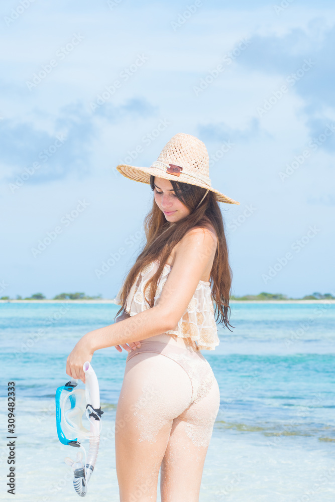 Young woman with wet skin looking down at tropical beach holding mask snorkel with hand