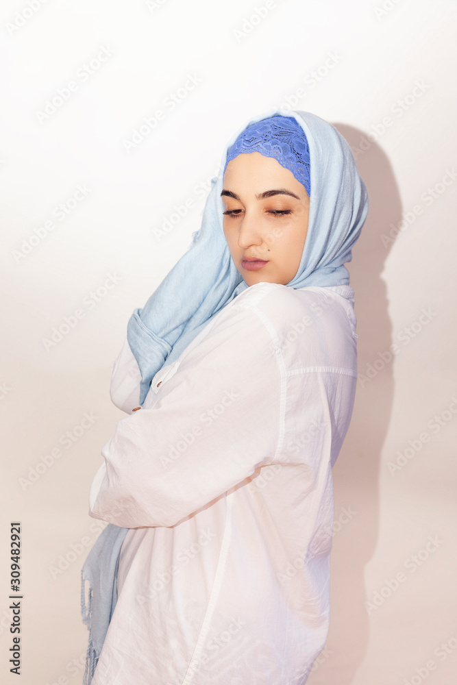 Elegant Muslim woman in white shirt and bright blue hijab. Stylish Iranian girl in Muslim clothing. Isolated portrait of attractive middle-eastern woman Elegant Muslim woman in white shirt and bright blue hijab. Stylish Iranian girl in Muslim clothing. Isolated portrait of attractive middle-eastern woman