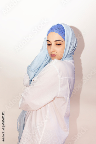 Elegant Muslim woman in white shirt and bright blue hijab. Stylish Iranian girl in Muslim clothing. Isolated portrait of attractive middle-eastern woman