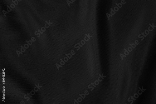 Black colored Background of soft draped fabric. Beautiful satin silk textured cloth for making clothes and curtains. Textile background texture.