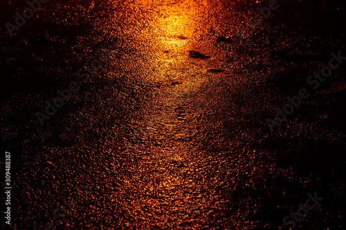 A wet pavement illuminated in the glow of lights at night