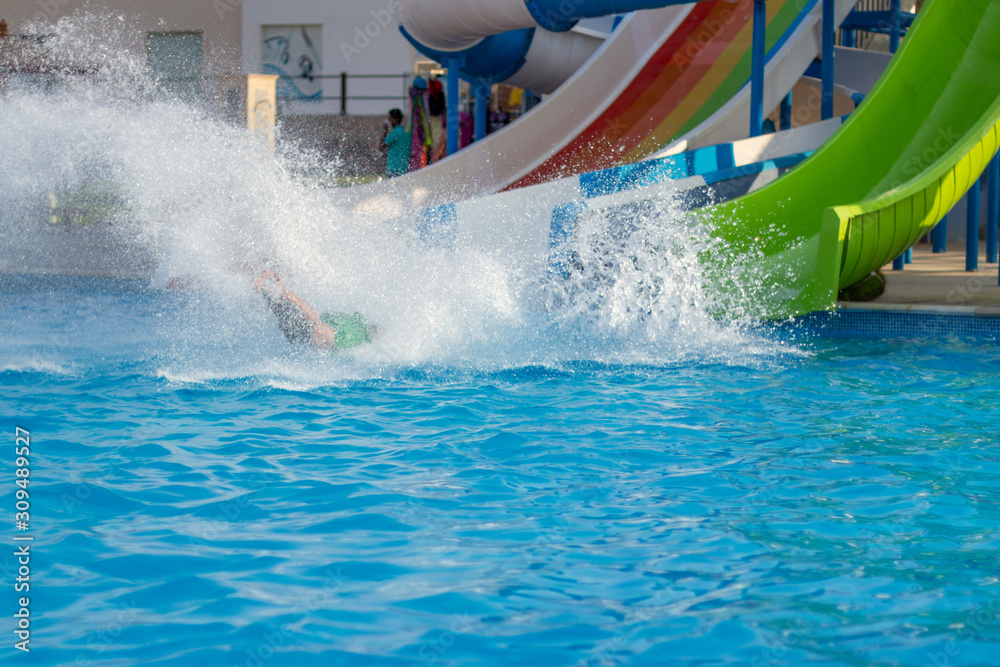 Obraz premium Happy cheerful people splashing water on water slide at aqua park..