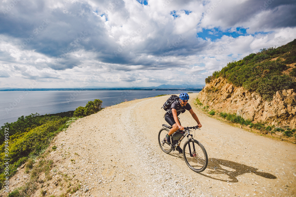 young guy riding a mountain bike on a bicycle route in Spain. Athlete on a mountain bike rides off-road against the background of the Mediterranean Sea, Costa Brava. Cycling in Spain