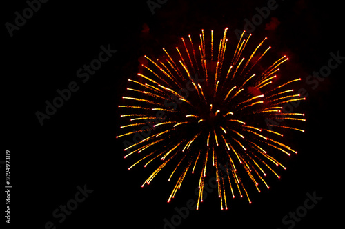 Yellow and red fireworks in the shape sphere on the right side on a black background.