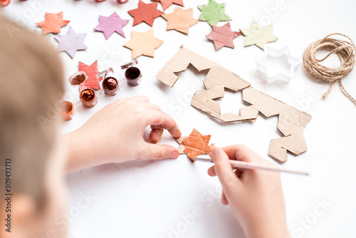 A child carves a star from cardboard. Christmas decoration, Christmas garland, hand made and Zero waste. Hands of a child on a white background. Div