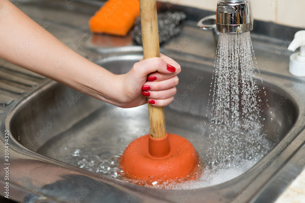 Woman Using Plunger In Kitchen Sink Stock Photo