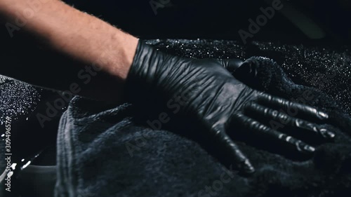 Using rag in palm of your hand, drops are removed from the car. Drop flow down the hood. Close up view of bonnet car. Process of polishing and washing auto. Hose is poured over cowl with water.