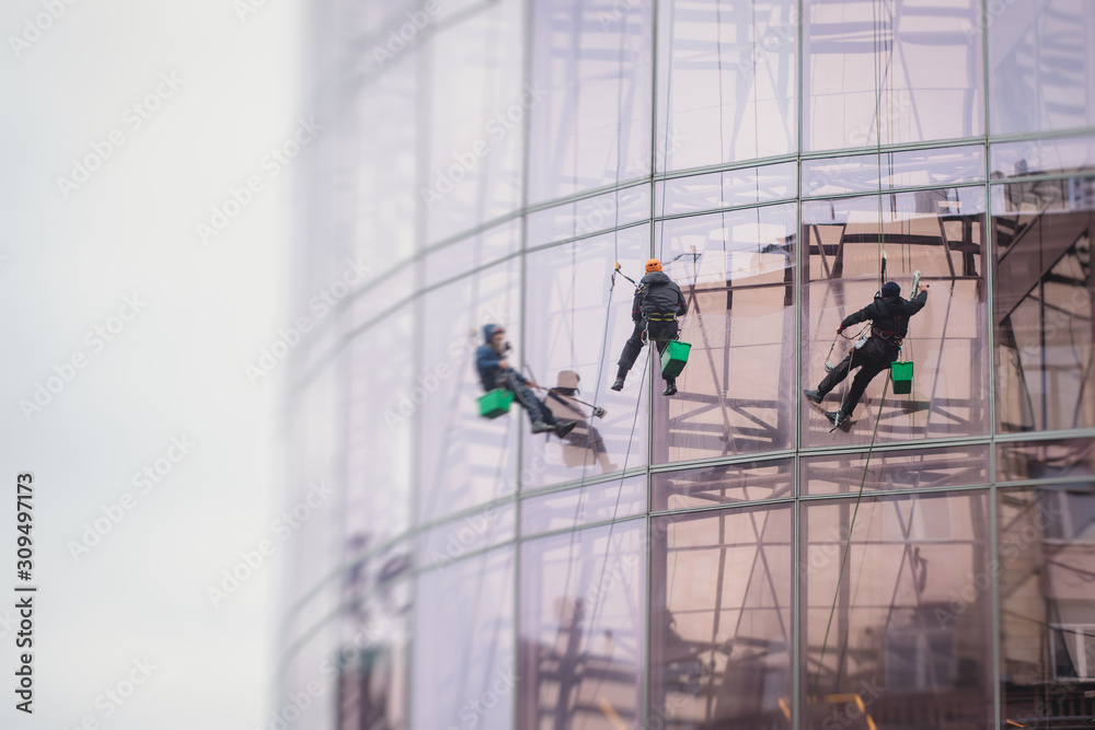 Group of workers cleaning the windows on the high rise building, industrial mountaineers washing the glass facade of a modern office building