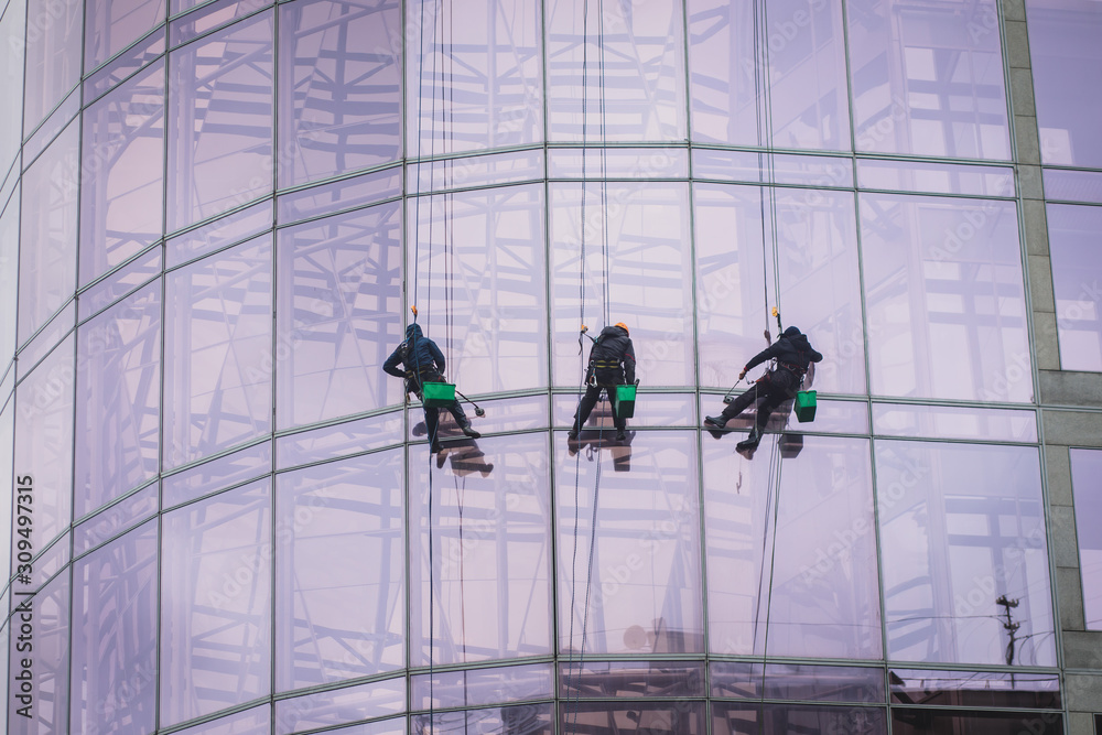 Group of workers cleaning the windows on the high rise building, industrial mountaineers washing the glass facade of a modern office building
