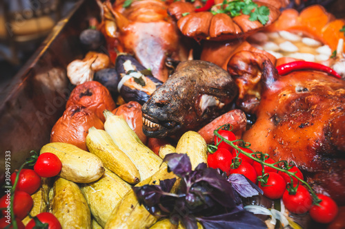 Big giant dish plate with roasted full pig pork head, served in restaurant with variety of vegetables and different meat assortment - lamb, ham and chicken.