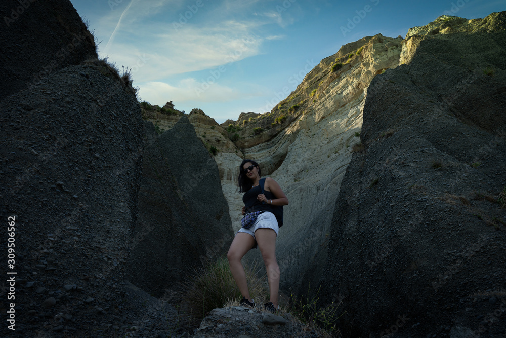 Young latin woman posing on a grotto, a big wall of rock and clay can be seen behind. Natural cliffs