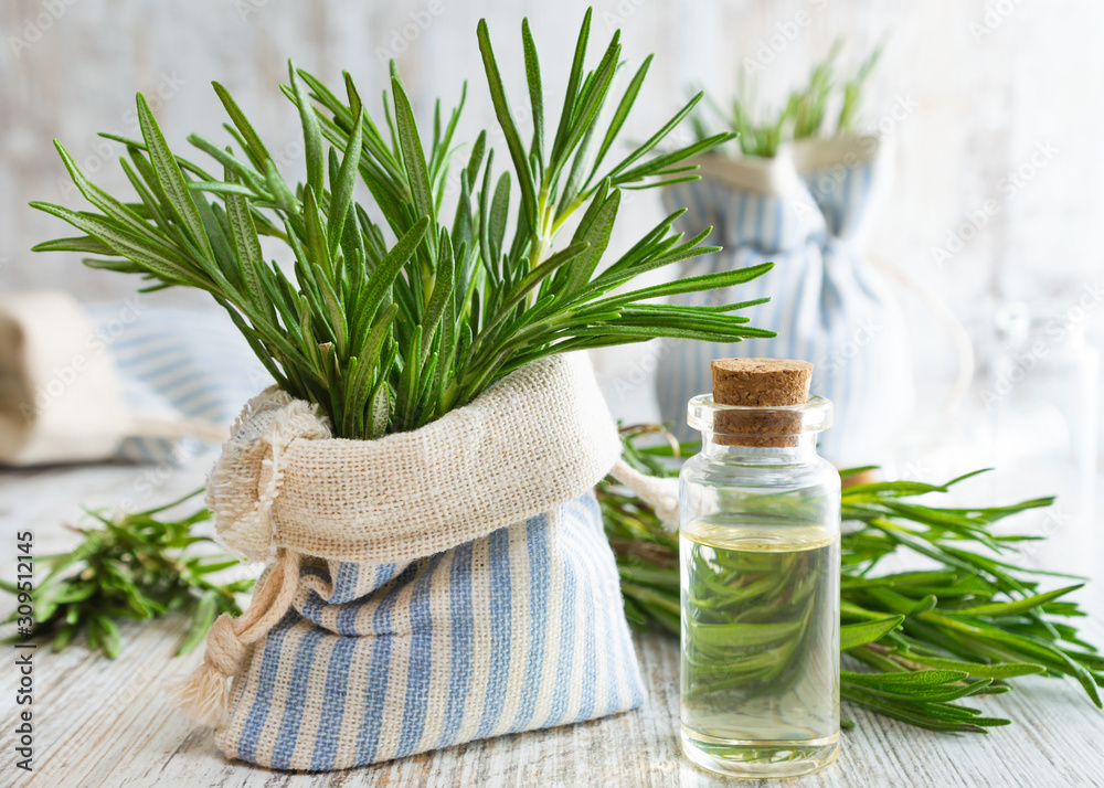 Rosemary essential oil and fresh rosemary in decorative pouch on old wooden table. - obrazy, fototapety, plakaty 