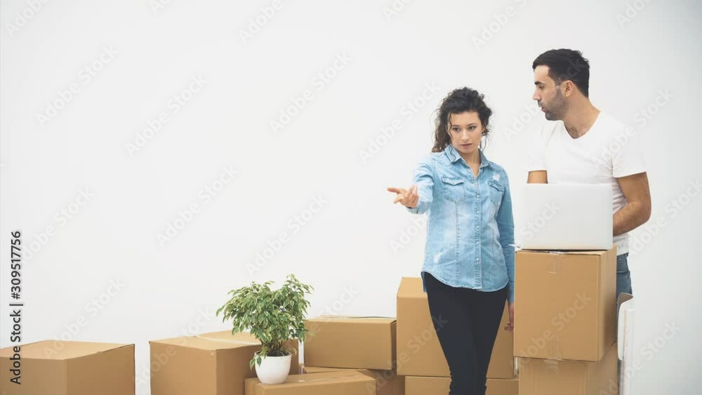 Young couple is moving to a new apartment together. They are thinking what to start from, looking at the screen of laptop. 4K.
