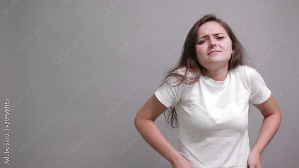Unhappy caucasian young woman in fashion white shirt keeping hand on belt, having pain in muscules isolated on gray background in studio. People sincere emotions, lifestyle concept. Unhappy caucasian young woman in fashion white shirt keeping hand on belt, having pain in muscules isolated on gray background in studio. People sincere emotions, lifestyle concept.