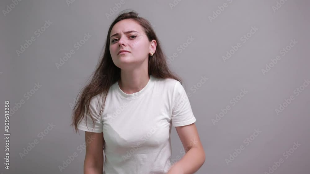 Serious caucasian young woman in fashion white shirt keeping hand near ear, listening, gossipgirl isolated on gray background in studio. People sincere emotions, lifestyle concept. Serious caucasian young woman in fashion white shirt keeping hand near ear, listening, gossipgirl isolated on gray background in studio. People sincere emotions, lifestyle concept.
