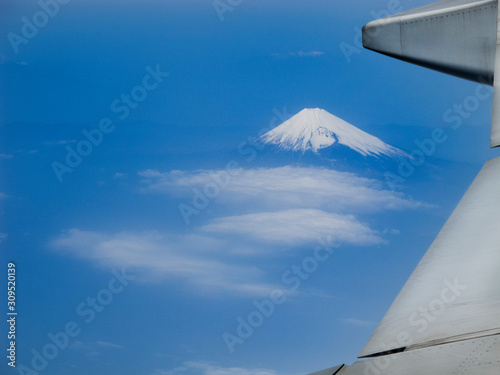 wing of airplane flying above clouds with volcano mountain