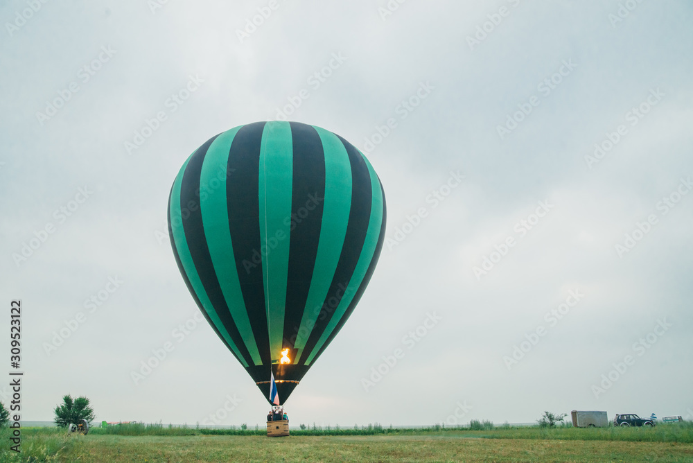 Obraz premium Inflating, unpack and flying up hot air balloon watermelon. Burner directing flame into envelope. Take off aircraft fly in morning blue sky. Start hot air burning to inflate gas fire to air balloon.