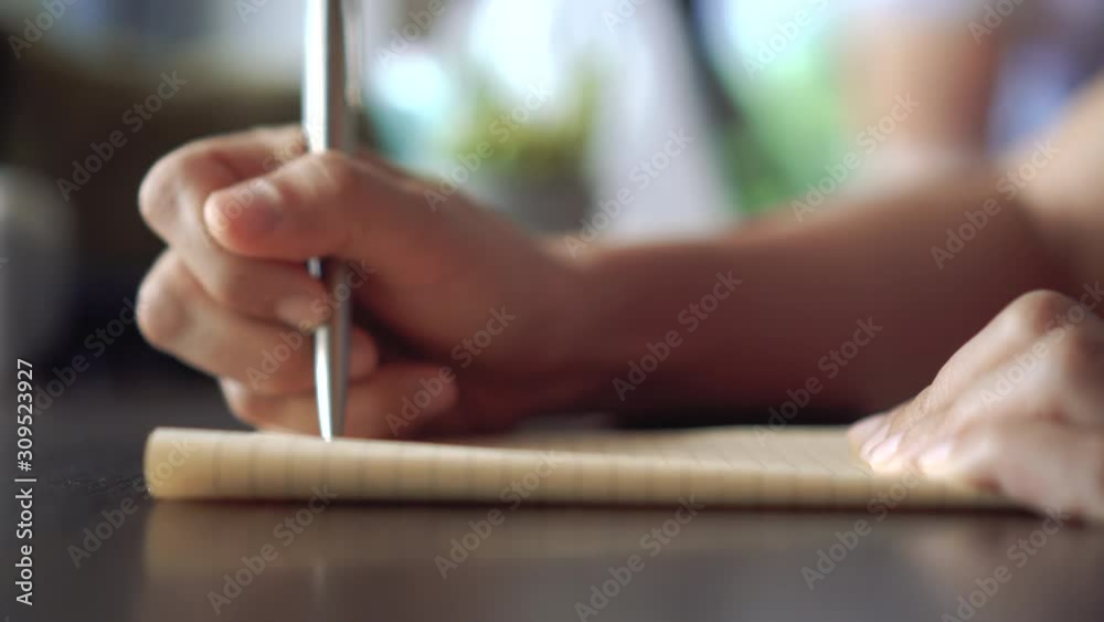 4K video copy space of  man hand writing down in white notebook with bokeh light in cafe background.