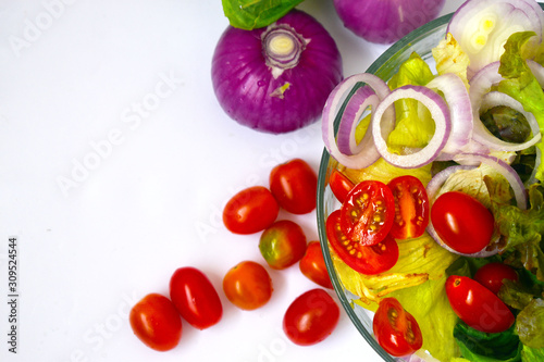 Group of organic vegetable, red onion, tomato, green leaves mixed in glass  bowl isolated on white background