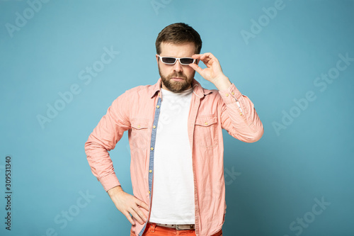 Serious bearded man in sunglasses looks confidently. Isolated on a blue background. © koldunova