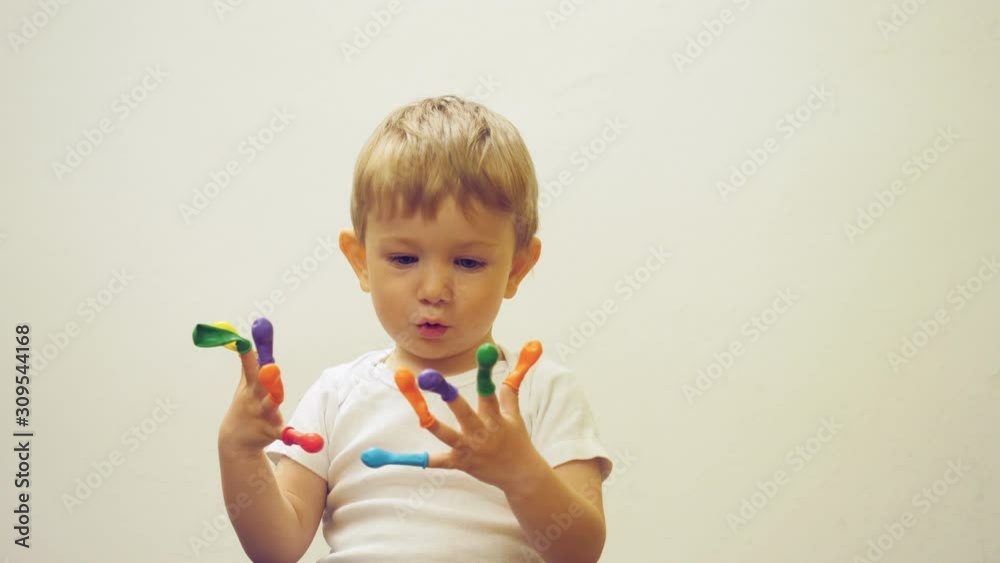 Funny child with blue eyes play with colored balloons on fingers Funny child with blue eyes play with colored balloons on fingers