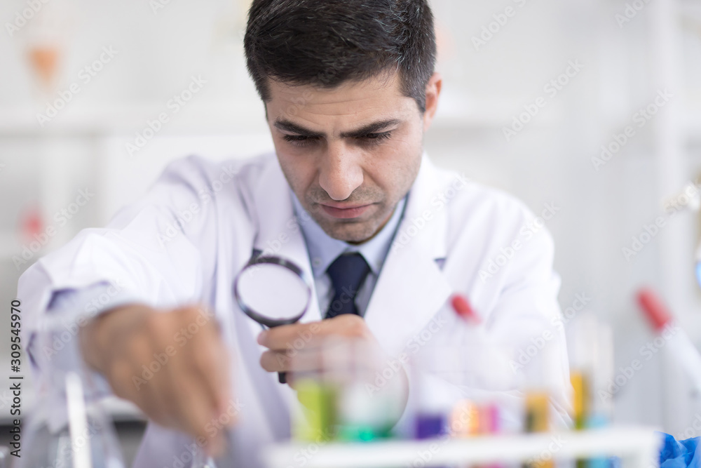 A male scientist with a magnifying glass looking at a science test tube in a research laboratory