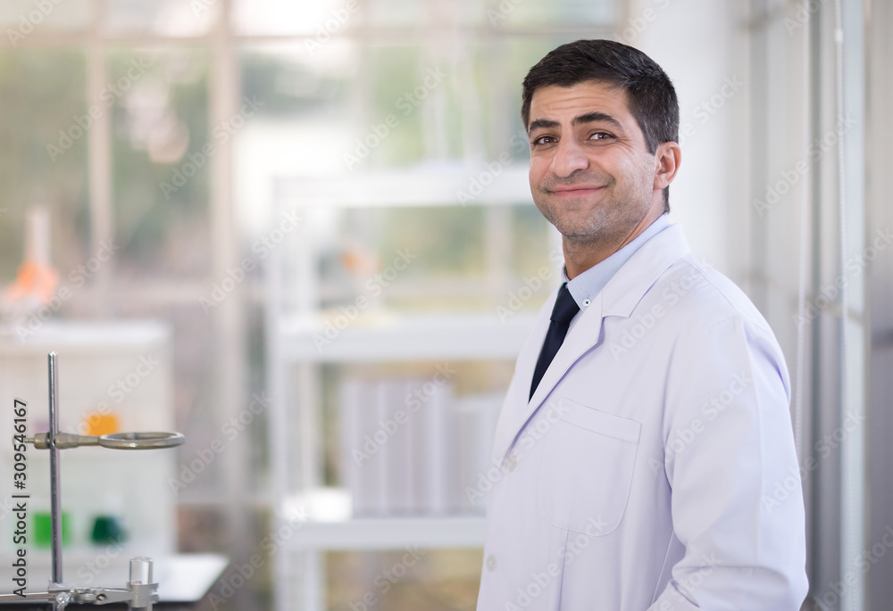 Handsome medical doctor in white coat is looking at camera and smiling while standing in laboratory