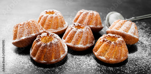 Mini bundt cakes or muffins with icing sugar on black wooden background.