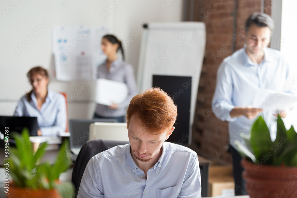 Employees working in shared office focus on busy redhead man Employees working in shared office focus on busy redhead man
