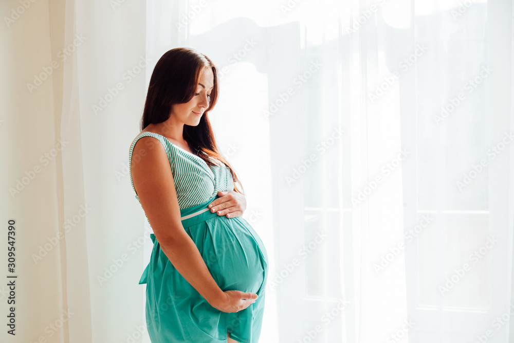 pregnant woman in a white room stands at the window pregnant woman in a white room stands at the window
