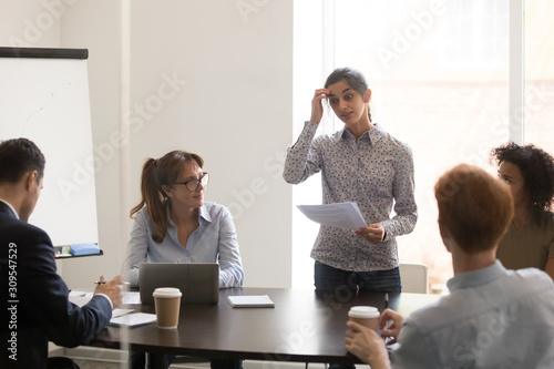 Indian presenter speaker stands in front of colleagues in meeting photo