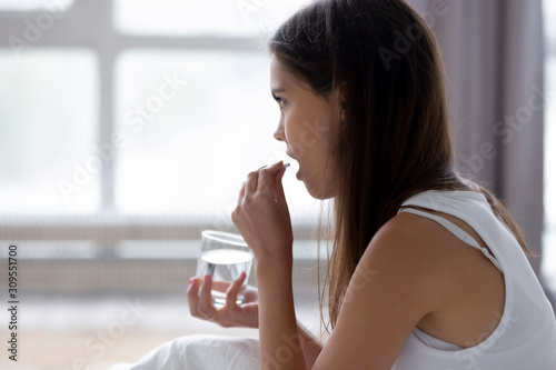 Young woman sit in bed talking pill drinking water