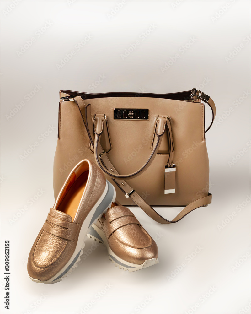 Beige women’s bag and a pair of pink gold beads on a light background