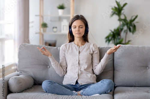 Calm young woman in headphones meditate on couch