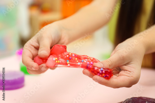 Little girl playing with red slime indoors, closeup photo