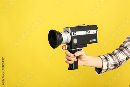 Woman with vintage video camera on yellow background, closeup of hand