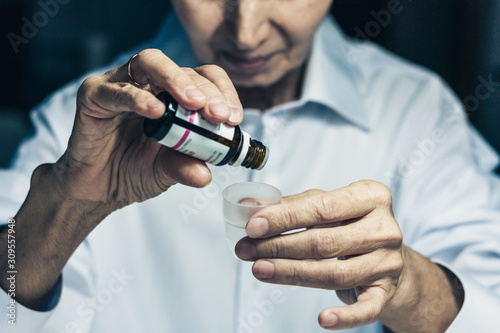 old woman hands close up holding medicine bottle and puts drops in a glass  healthcare concept background with copy space.