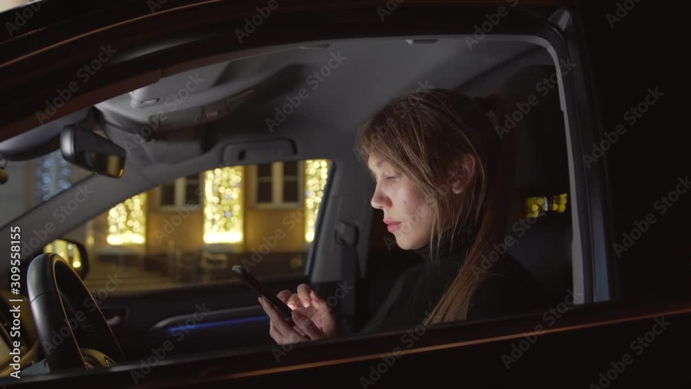 Attractive woman in a black car in a driver seat checking her smartphone Attractive woman in a black car in a driver seat checking her smartphone