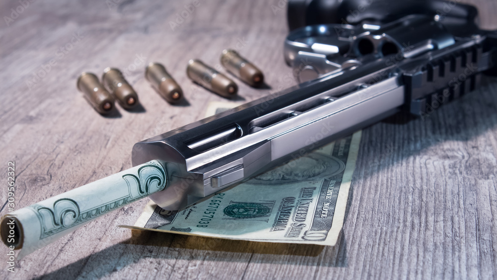 Naklejka premium A pistol with bullets and money dollars lies on wooden the table. Revolver close-up.