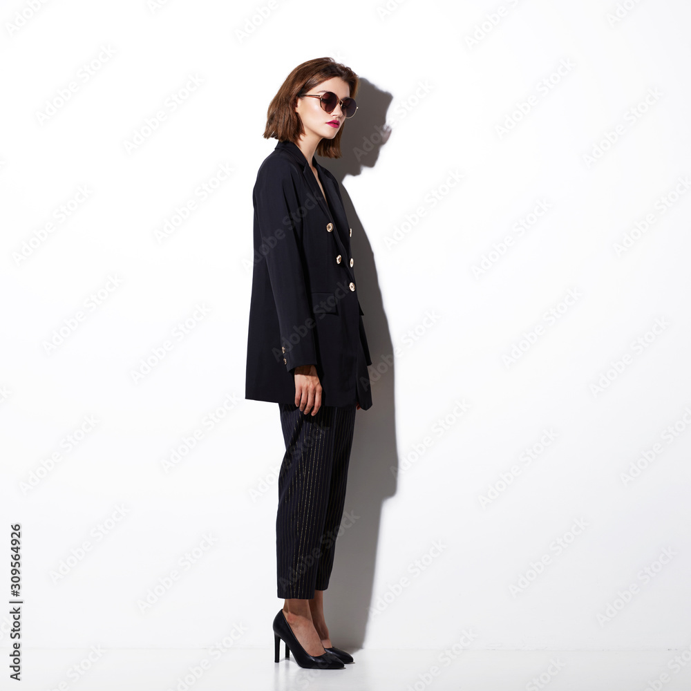 High fashion portrait of young elegant woman. Sunglasses, black jacket, pants.