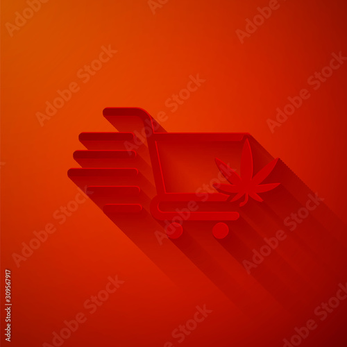 Paper cut Shopping cart with marijuana or cannabis leaf icon isolated on red background. Online buying. Delivery service. Supermarket basket. Paper art style. Vector Illustration