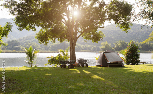 Tourist tent in forest camp among meadow. Camping green tent in forest near lake.