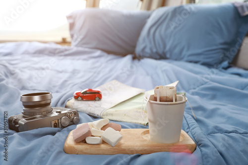 Cup of coffee with marshmallows, camera and map on bed in caravan.