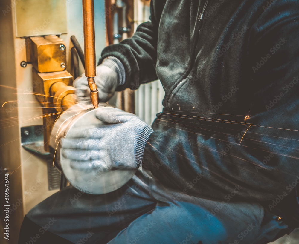 Welder in gloves is working at spot welding machine. Welding of pipes for chimneys. Welder in gloves is working at spot welding machine. Welding of pipes for chimneys.