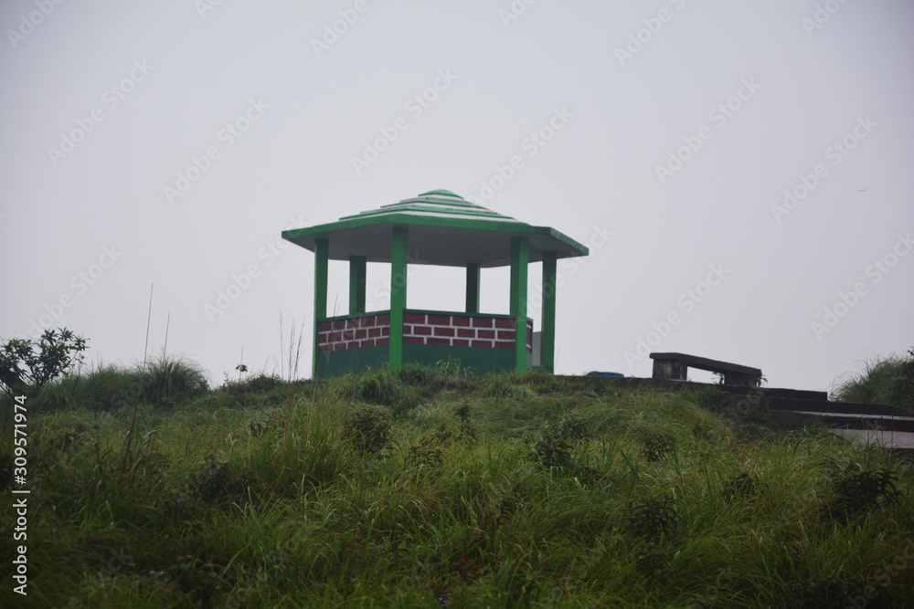 The famous concrete shed or Gazebo or pavilion of Cherrapunjee Eco park with 1/3 brick wall, pillars and roof, stone path and green grasses and foggy sky, selective focusing