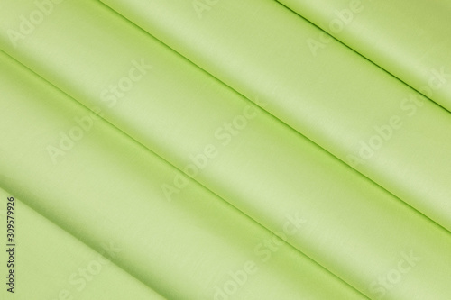 The green satin fabric is laid out on the table. Soft folds of material drapery have pronounced diagonal direction