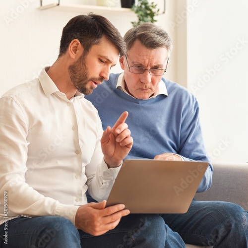 Mature Son Explaining Father How To Use Laptop Sitting Indor