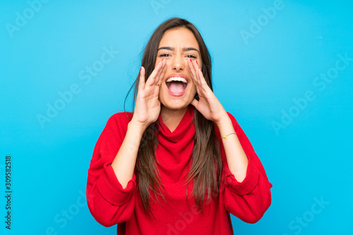 Young woman with red sweater over isolated blue background shouting with mouth wide open