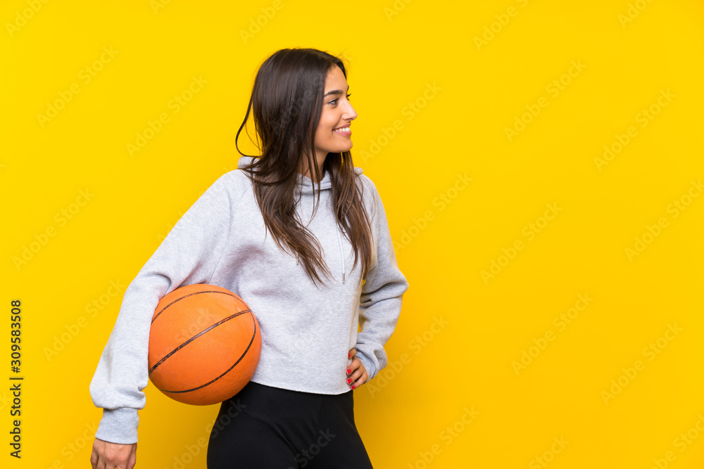 Young woman playing basketball over isolated yellow background Young woman playing basketball over isolated yellow background