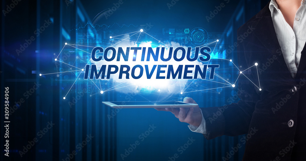Young business person working on tablet and shows the inscription: CONTINUOUS IMPROVEMENT Young business person working on tablet and shows the inscription: CONTINUOUS IMPROVEMENT
